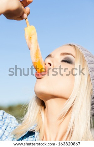 Close-up of beautiful blond girl with smokey eye make up who enjoys sucking ice cream with her plump sexy passionate lips on sunny summer day