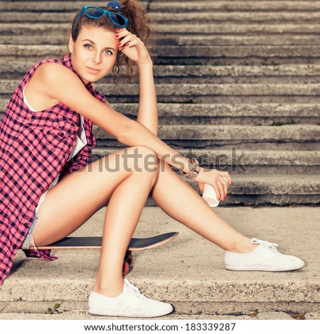 beautiful young girl holds white to-go cup sits on skateboard on stone stairs