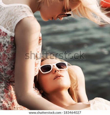 beautiful blonde girl looks at her tanned girlfriend in sunglasses who lies on her knees under water
