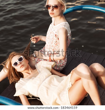 one beautiful girl lies on her girlfriend\'s knee holding to-go cup while her friend plays with her hair