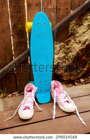 Pink converse sneakers with untied laces on a wooden floor near blue pennyboard skateboard longboard with multi color wheels. Urban hipster outfit