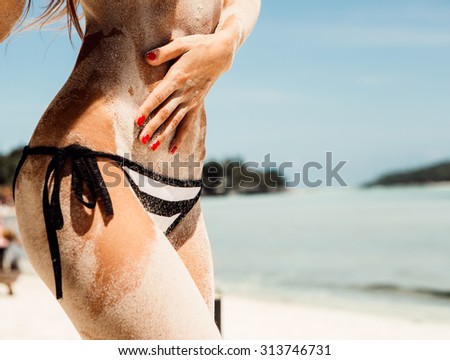 Sandy abs and butt of a young beautiful sporty lady in striped black and white bikini panties on the tropical sea shore background. Outdoor lifestyle picture on a hot sunny summer day.