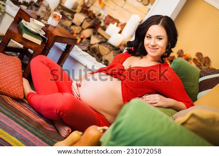 Happy pregnant woman in a red clothes sitting by the fireplace in the autumn interior