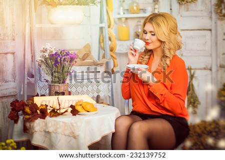 the blonde girl in the red blouse drinking tea in the autumn room interior