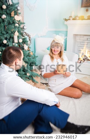 Is it for me? Cheerful young woman sitting on the carpet and receiving a gift box from her boyfriend sitting close to her