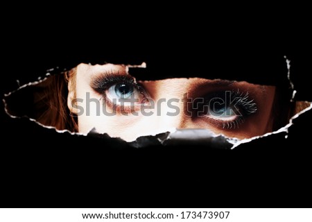 Blue eyes of young woman peeping through a hole closeup