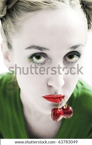 Face of a young beautiful green-eyed woman with cherries in the mouth