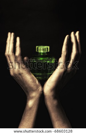 Men\'s hands in golden paint holding green bottle of perfume on black backgroun