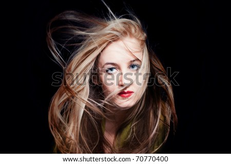Beautiful blue-eyed woman with hair fluttering in wind on black background, fashion look