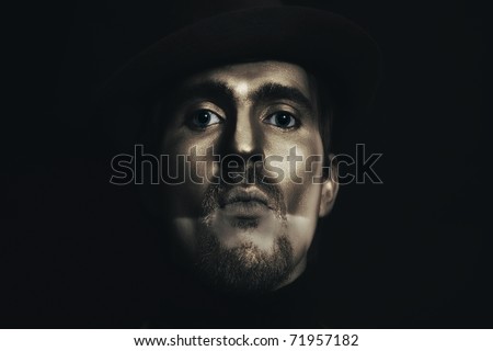 portrait of young attractive man in hat with bronze makeup on her face on black background