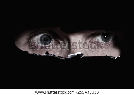 Scary eyes of a man spying through a hole in the wall