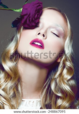 Beautiful face of a glamour woman with pink lips make up. Dark background. The rose lies on the right eyes