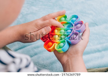 Boy playing with rainbow pop it fidget toy. Push bubble fidget sensory toy - washable and reusable silicon stress relief toy. Antistress toy for child with special needs. Mental health concept