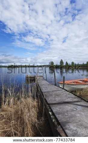 Pier leading to a lake, nice blue sky and a fishing boat ready to use