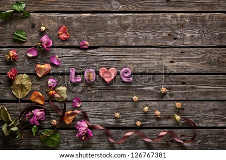 Sweet holiday background with word Love rose petals, curved ribbon on old wood.