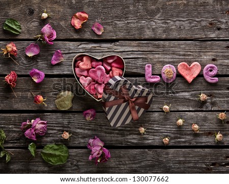 Word Love with heart shaped Valentines Day gift box on old vintage wooden plates. Sweet holiday background with rose petals and dried rose flowers.