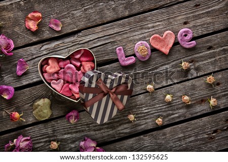 Word Love with heart shaped Valentines Day gift box on old vintage wooden plates. Sweet holiday background with rose petals and dried rose flowers.