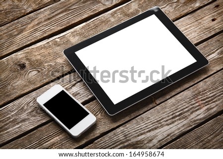 Digital tablet computer and white smart phone with isolated screens on old wooden desk.