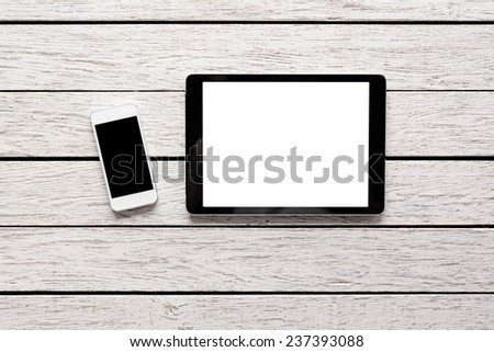 Tablet computer and white smart phone with isolated screens on white wooden desk.