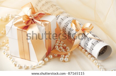 Gift box and sheets of musical notes tied with gold ribbon and pearl necklace.