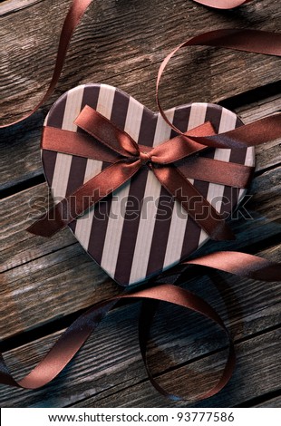 Heart shaped Valentines Day gift box with curved ribbon on old wood. Vintage holiday background.