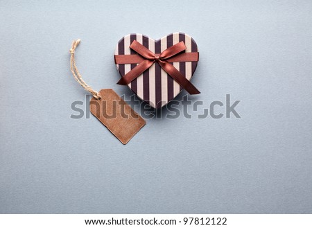 Heart shaped Valentines Day gift box with blank gift tag on a soft blue paper background.