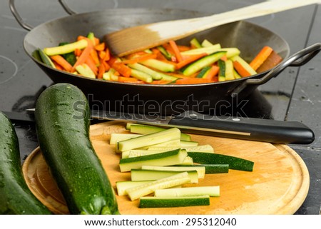 Cooking of stir-fried vegetables with zucchini and carrots. Focus on cutting board in foreground.