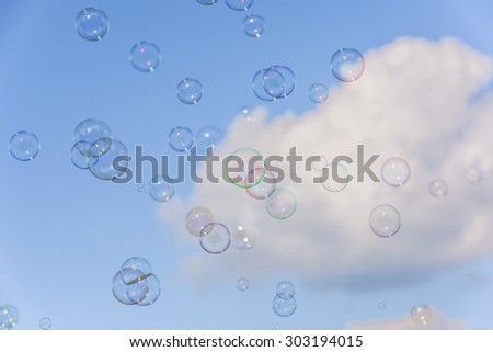 A bunch of colorful soap bubbles flying up into the blue, cloudy sky.