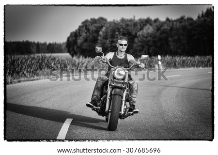 Tough guy with sparrow beard, undercut and blue jeans in motion on the road on a chopper bike