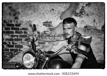 Tough guy with sparrow beard, undercut and blue jeans sitting on a chopper bike in front of  a weathered brick wall