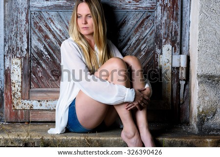 Blond woman in hot pants sitting in front of an weathered door
