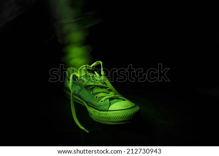 Single old fashionable toxic training shoe in green light at night with visible odor