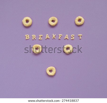 Word Breakfast Written With Pink Pasta Letters on violet background with cereal rings