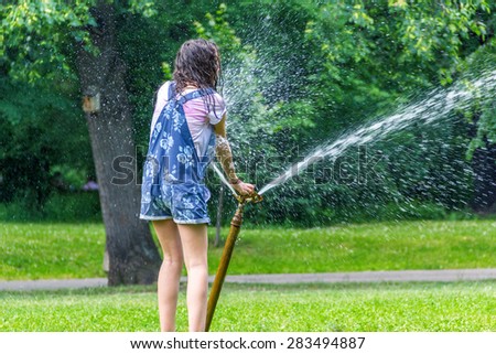 Children play with automatic sprinkler watering in garden in summer