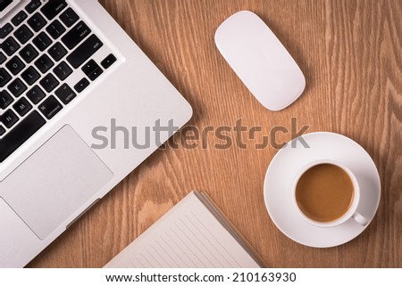 Notepad, laptop and coffee cup on wood table. View from above