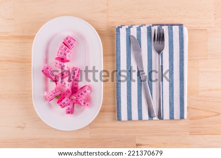 Empty plate with measure tape, knife and fork. Diet food on wooden table. Weight loss concept