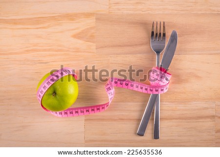 Plate with measure tape, knife and fork. Diet food on wooden table. apple and measuring tape on the floor scales isolated on white