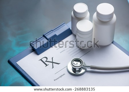 Empty medical prescription with a stethoscope and medicine bottles on blue reflective background