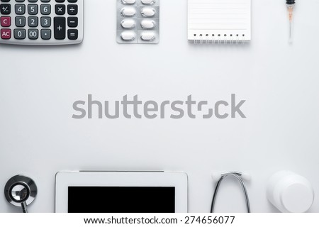 Modern medicine workplace with digital tablet, notepad, stethoscope, calculator, bottles, pills and syringes at doctor\'s desk. Copy space view from the top