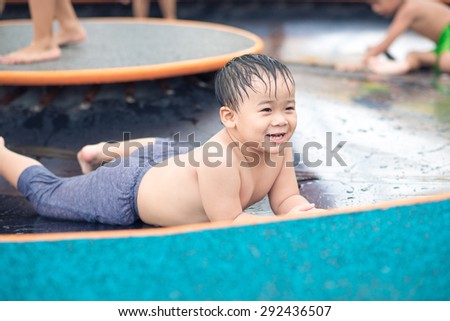 A super happy child is laying in a small wading pool, looking up at the camera and smiling. Empty space off to the side for text / copy space.