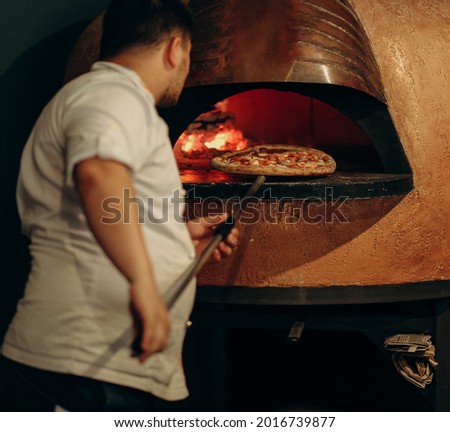 The chef prepares pizza in a wood-fired oven. Cooking pizza. The cook puts the pizza in the oven. Hot delicious pizza from the oven.
