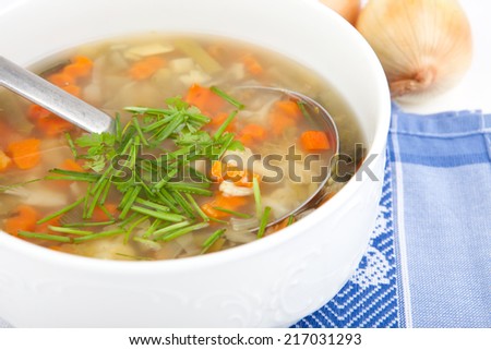 soup bowl full of fresh boiled vegetables, silver dipper inside, onion in background, closeup, aerial view