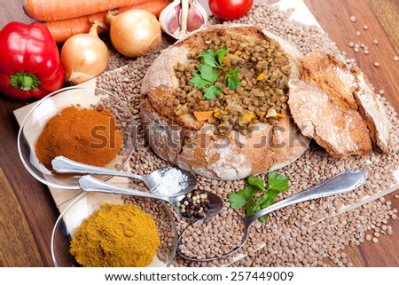 loaf of bread with lentil soup inside on wooden plate, with vegetables, indian curry spice