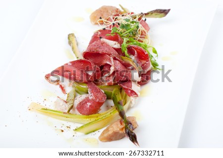 smoked duck breast slices with green marinated asparagus and sweet banana chutney on white plate