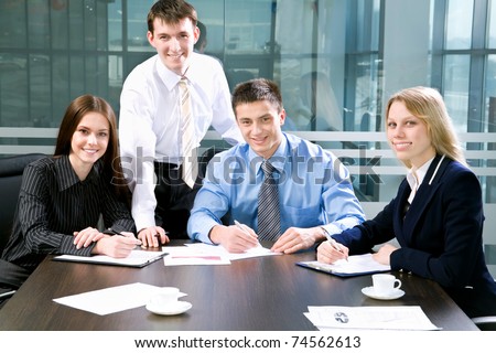 Four business colleagues sitting around table and working together, looking at camera, smiling