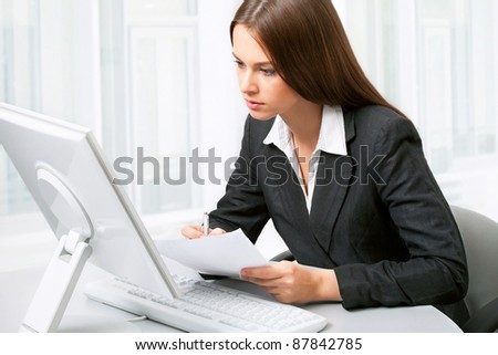 Image of pretty business woman sitting in front of computer and looking at its screen