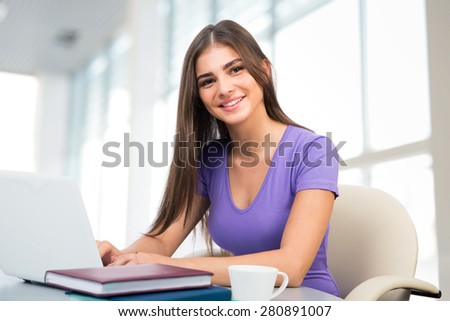 Pretty female student with laptop working in a high school library