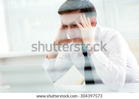 Businessman working at laptop in office. View through blinds