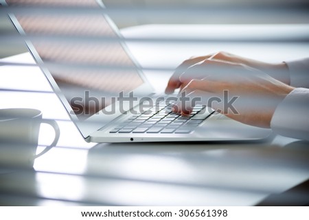 Close-up of hands of business man typing on a laptop. View through blinds
