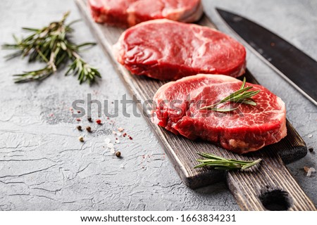 Three pieces of traditional thin steak cut from the tenderloin on wooden cutting board with olive oil, salt, rosemary and pepper. Raw Black Angus Prime meat steaks suitable for grilling or frying pan.